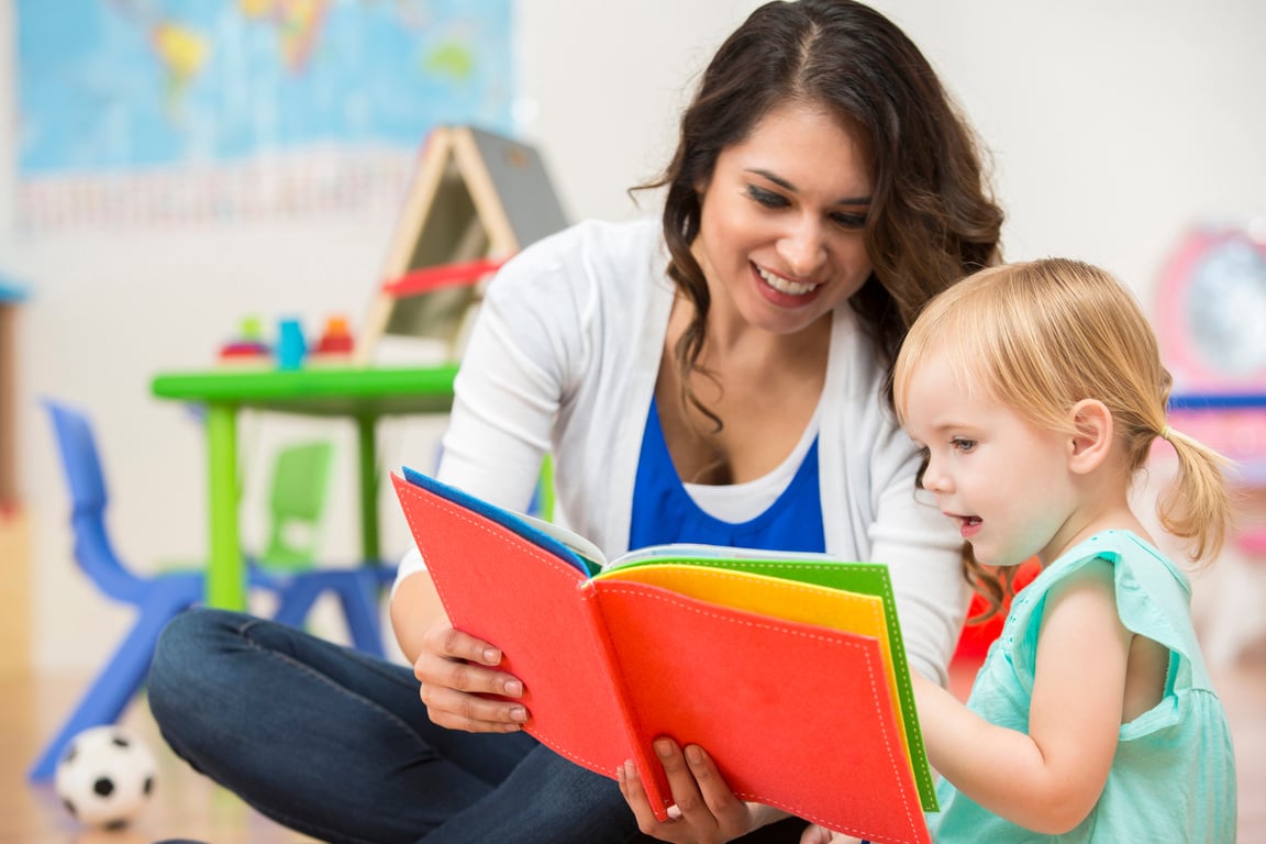 Hispanic preschool teacher reading a book to cute toddler girl